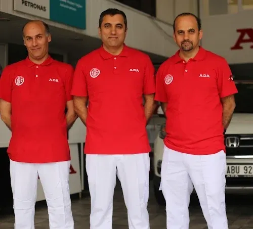 ADA Honda ekibinden üç teknisyen, kırmızı forma ile atölye önünde