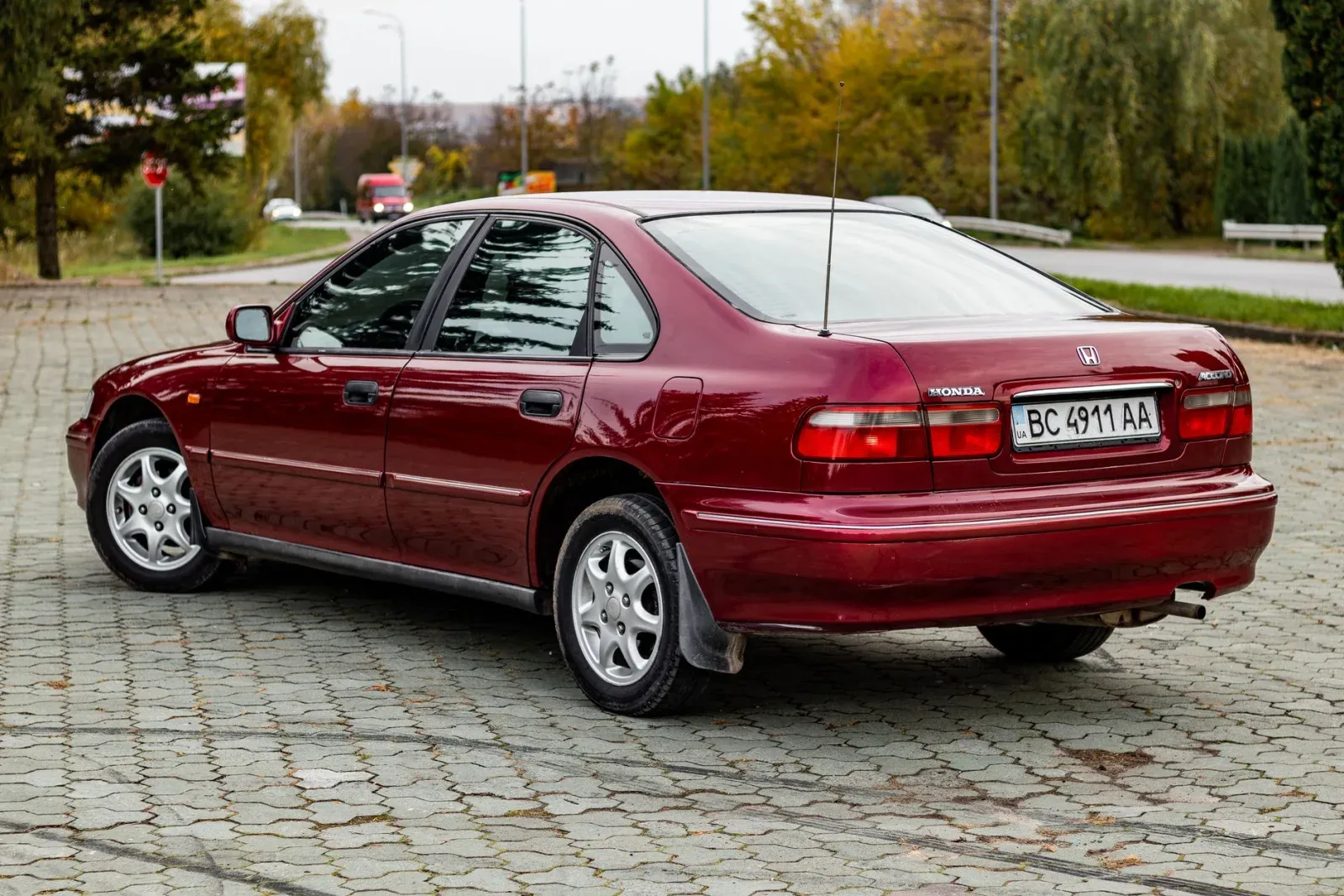 Bordo/kırmızı Honda Accord sedan, arka bagaj kapağında "HONDA" ve "ACCORD" yazıları net okunuyor, taş döşeli park alanında arkadan/yandan çekim