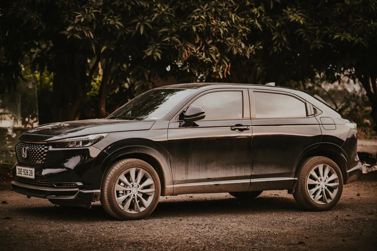 Siyah Honda HR-V crossover, ağaçların önünde yandan çekim, "H" logolu ön ızgara ve "RS" jant merkezi net görünüyor